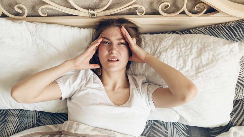 Frau liegt im Bett und hält sich den Kopf | Bild: picture alliance / Zoonar | Max 4e Frau liegt im Bett und hält sich den Kopf