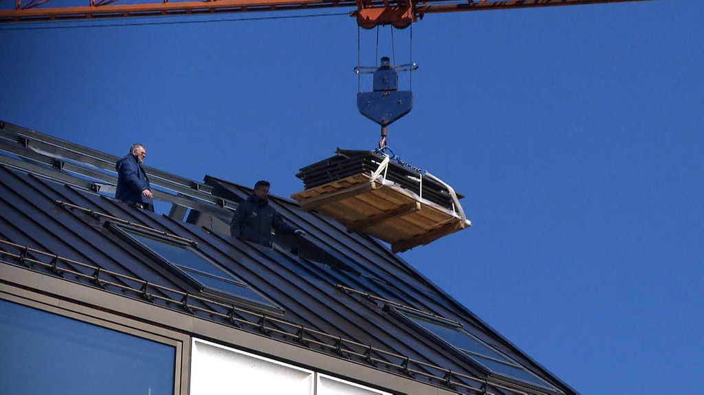 Arbeiter auf einem Dach, das gerade mit Hilfe eines Krans fertiggestellt wird.