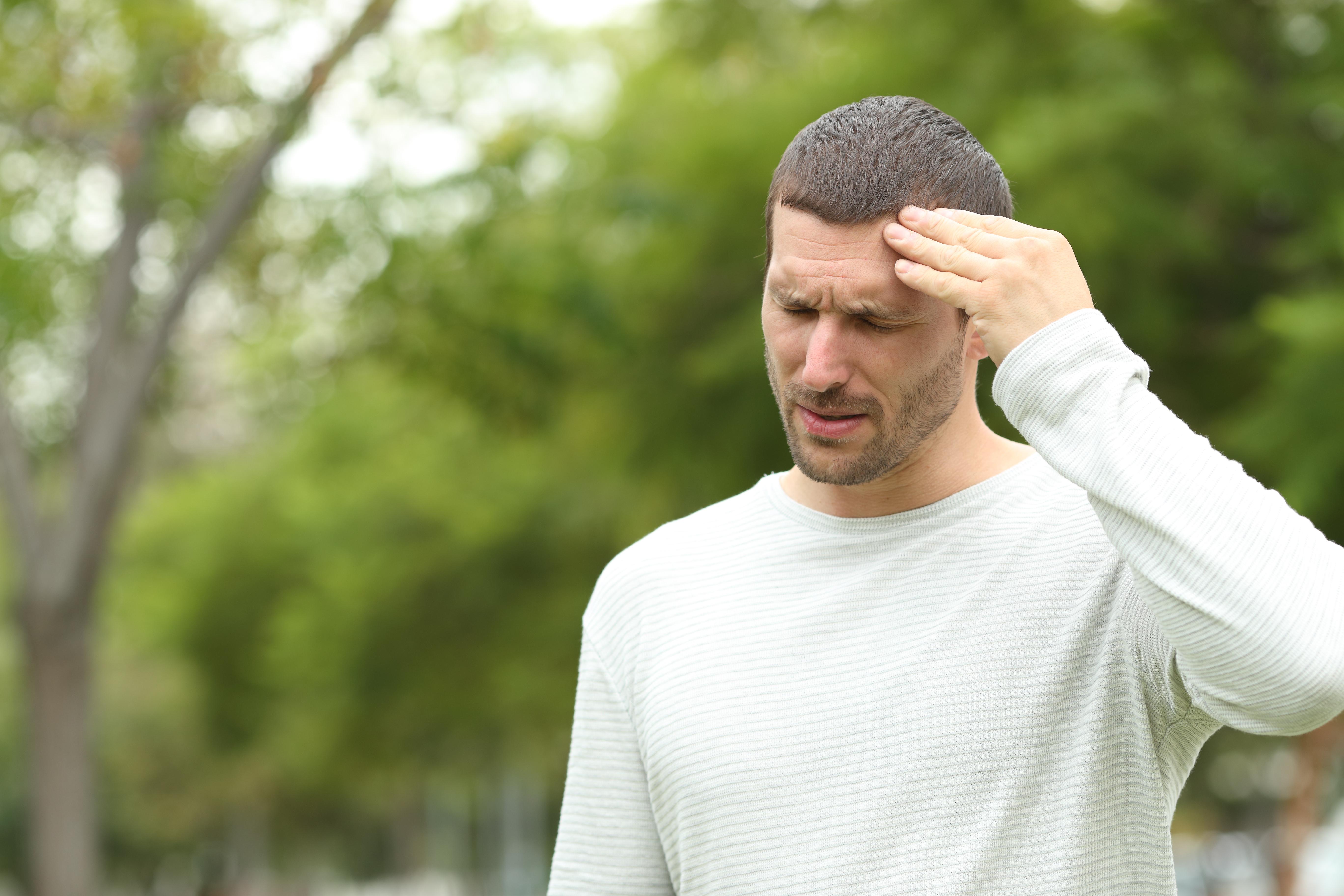 Mann in freier Natur, der sich den Kopf schmerzverzerrt hält.