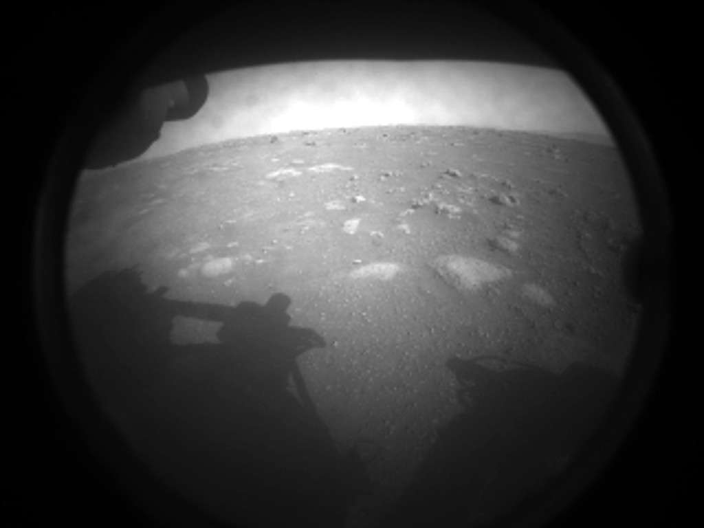 Ein schwarzweißes Bild zeigt einen kleinen Ausschnitt der Marsoberfläche, im Vordergrund ist der Schatten des Rovers Perseverance zu sehen. 