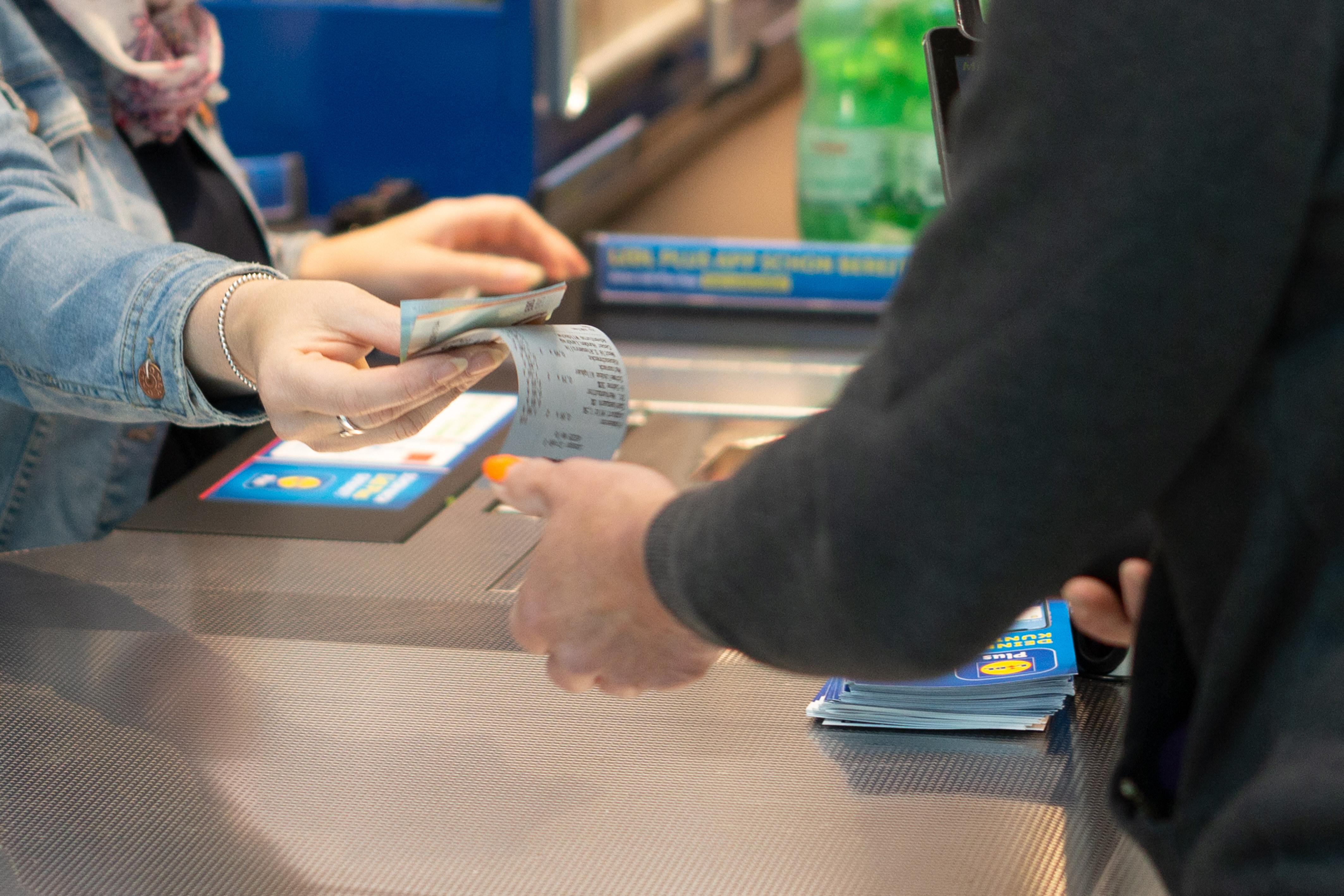 Ein Mitarbeiterin in einem Geschäft gibt dem Kunden sein Wechselgeld und den Kassenbon.