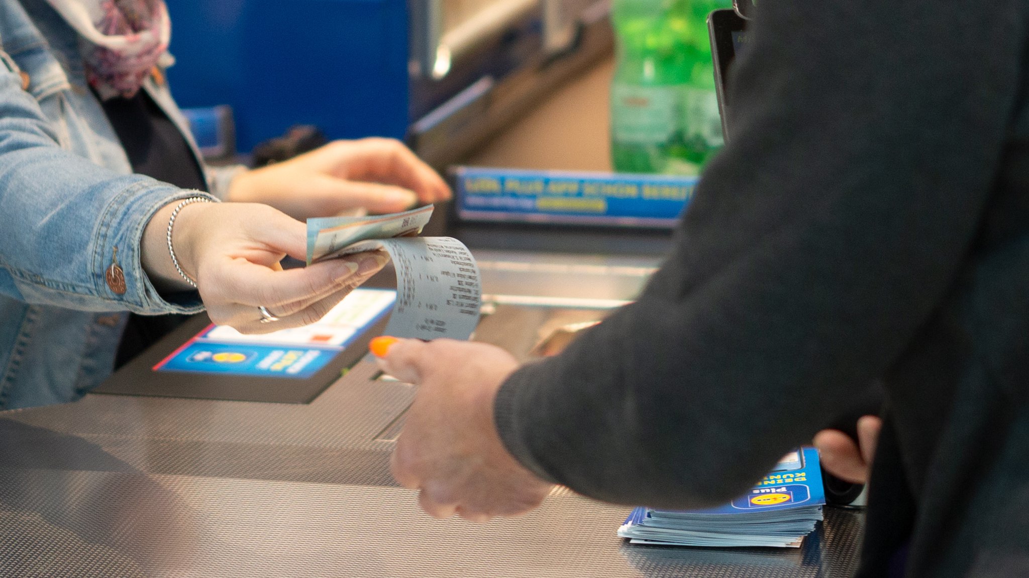 Ein Mitarbeiterin in einem Geschäft gibt dem Kunden sein Wechselgeld und den Kassenbon.