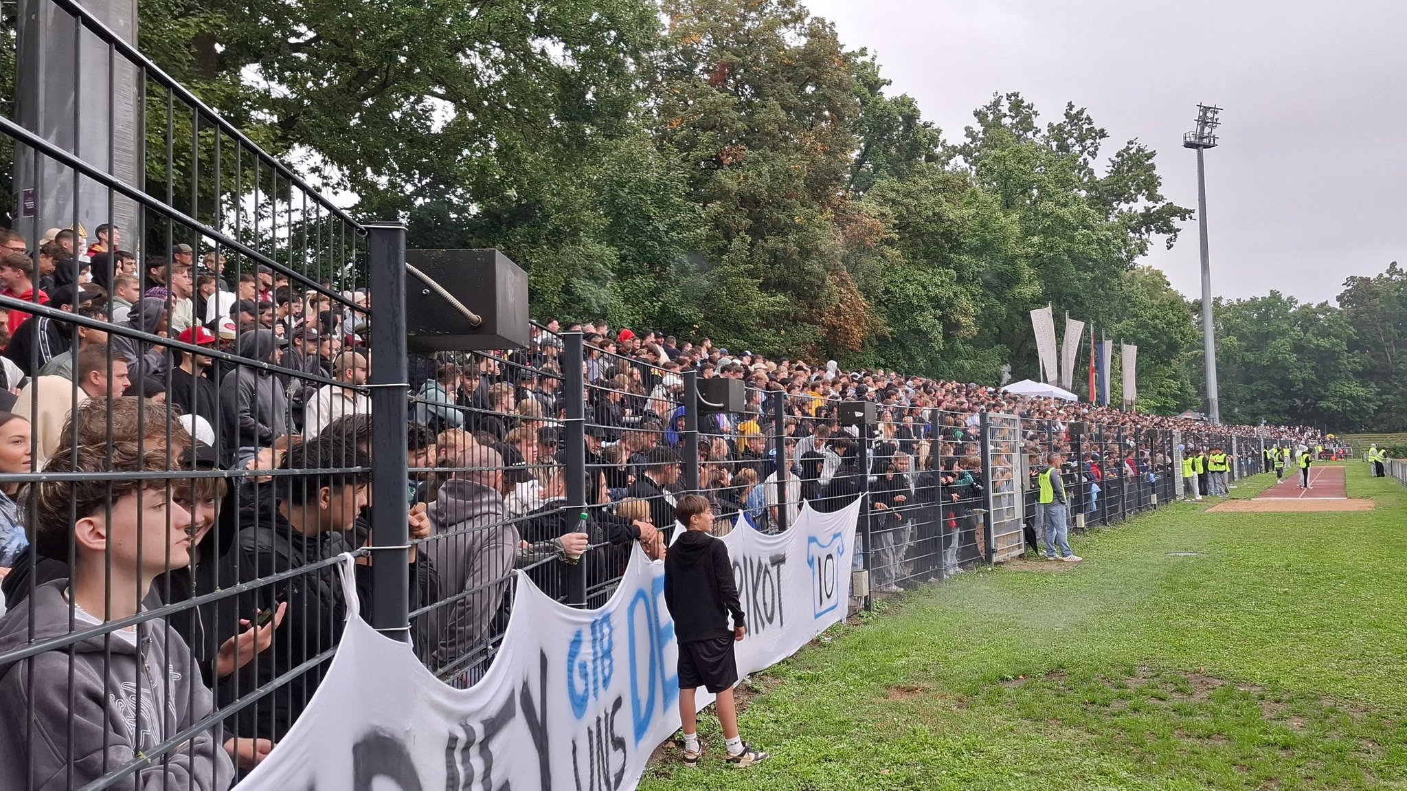 Fans auf einer Stehtribüne hinter einem Zaun 