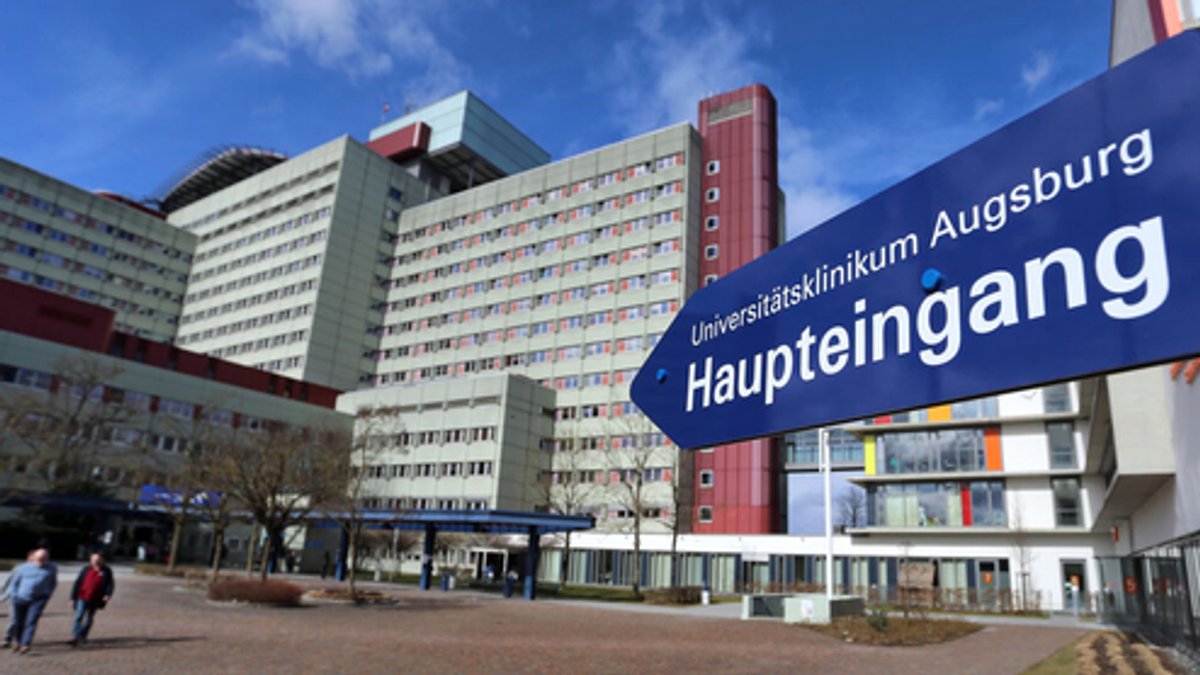 Blaues Schild mit weißer Schrift weist auf den Haupteingang des Universitätsklinikums Augsburg hin