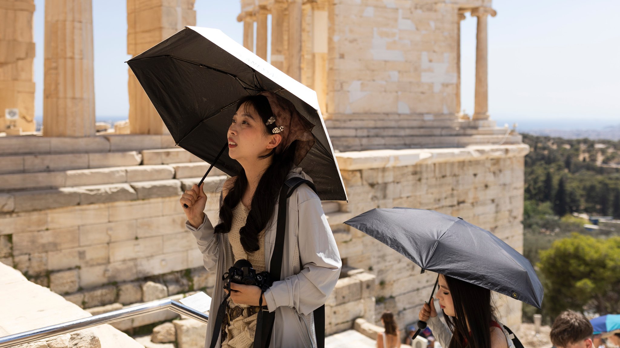 18.06.2024: Touristinnen suchen Schatten unter Schirmen während des Besuchs auf der Akropolis.