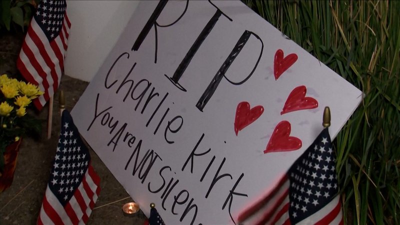Ein Schild mit der Aufschrift "RIP Charlie Kirk" und roten Herzen liegt zwischen US-Flaggen und Teelichtern auf dem Boden | Bild: BR Ein Schild mit der Aufschrift "RIP Charlie Kirk" und roten Herzen liegt zwischen US-Flaggen und Teelichtern auf dem Boden