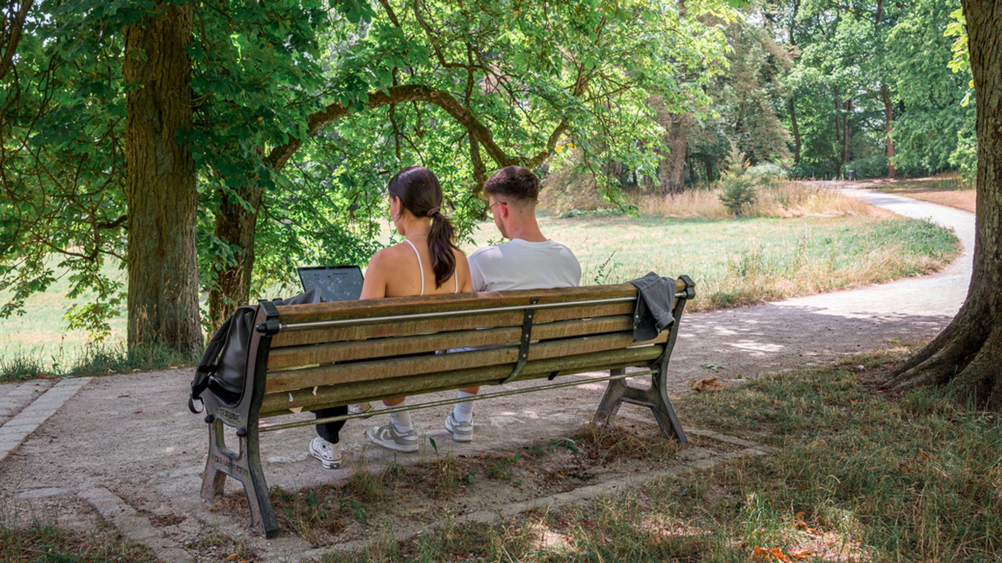 Zwei Personen sitzen am 15.7.23 im Hofgarten in Coburg im Schatten auf einer Bank. 