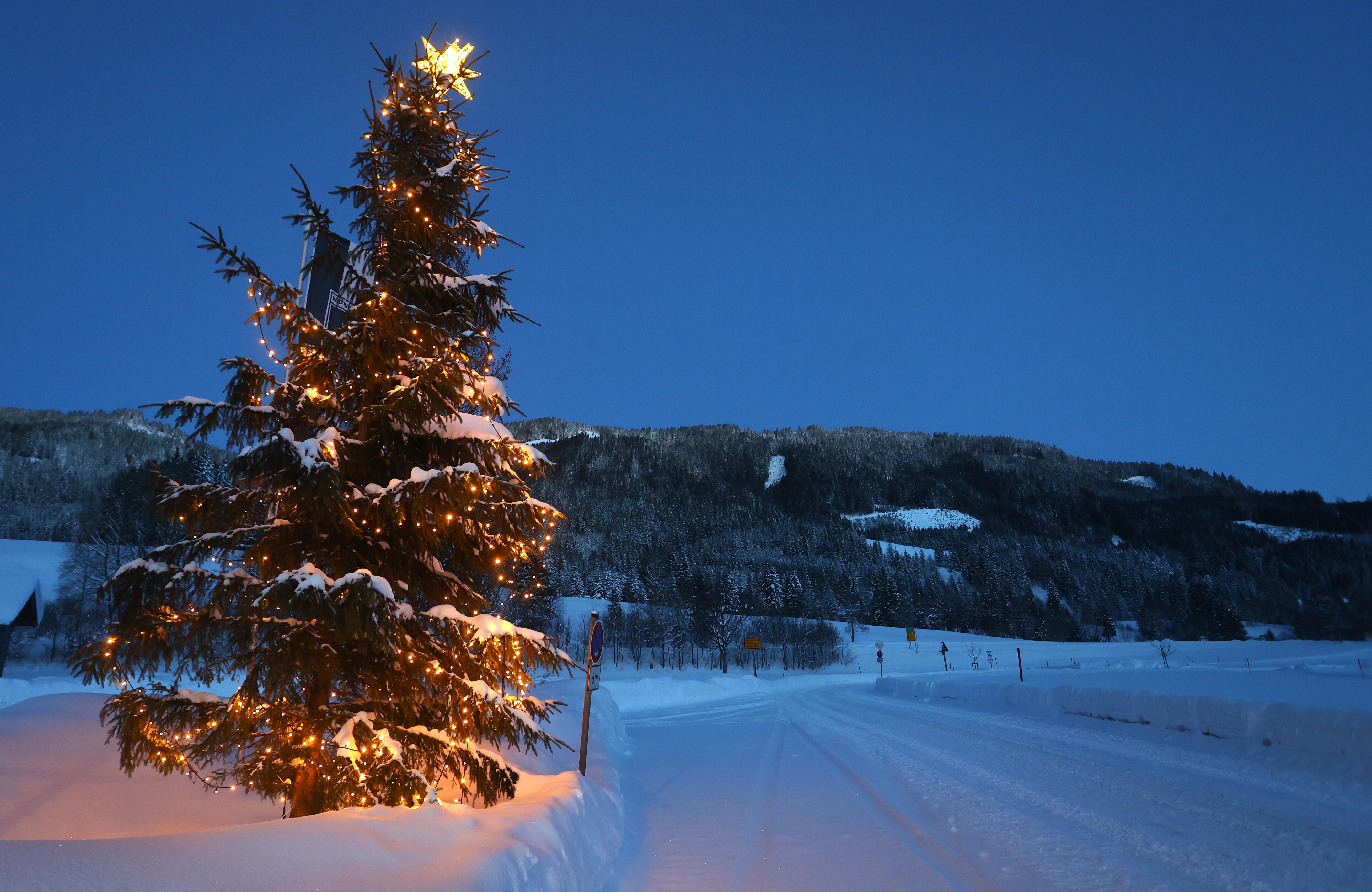 Ein geschmückter Weihnachtsbaum steht kurz vor Sonnenaufgang im Ortsteil Unterjoch in der schneebedeckten Landschaft.