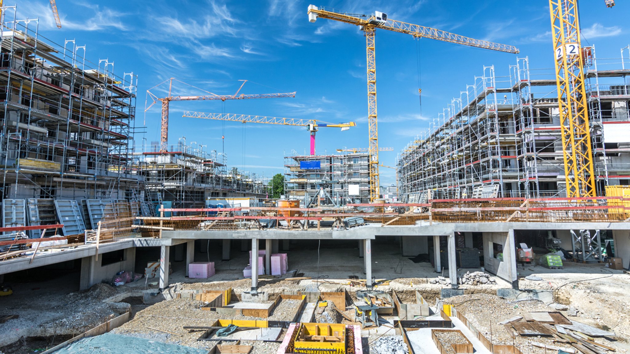 Großbaustelle mit Kränen, gelegten Fundamenten und eingerüsteten Rohbauten (Symbolbild)