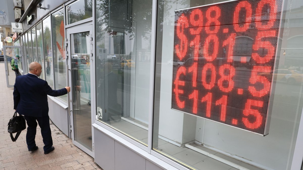 Mann betritt eine Bankfiliale, in deren Schaufenster Umtauschkurse angezeigt werden