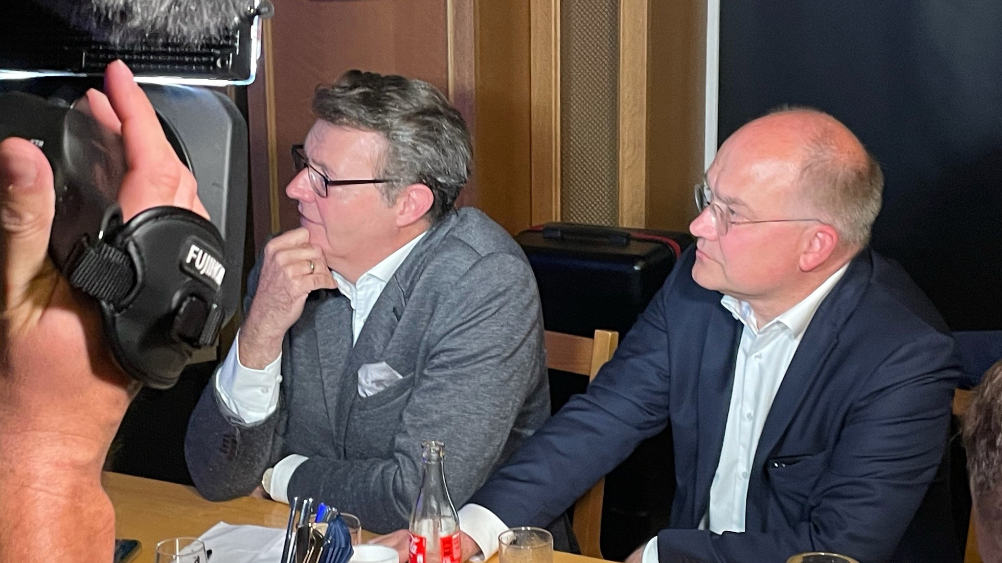 Michael Frieser und Sebastian Brehm sitzen am Tisch und schauen auf einen Bildschirm.