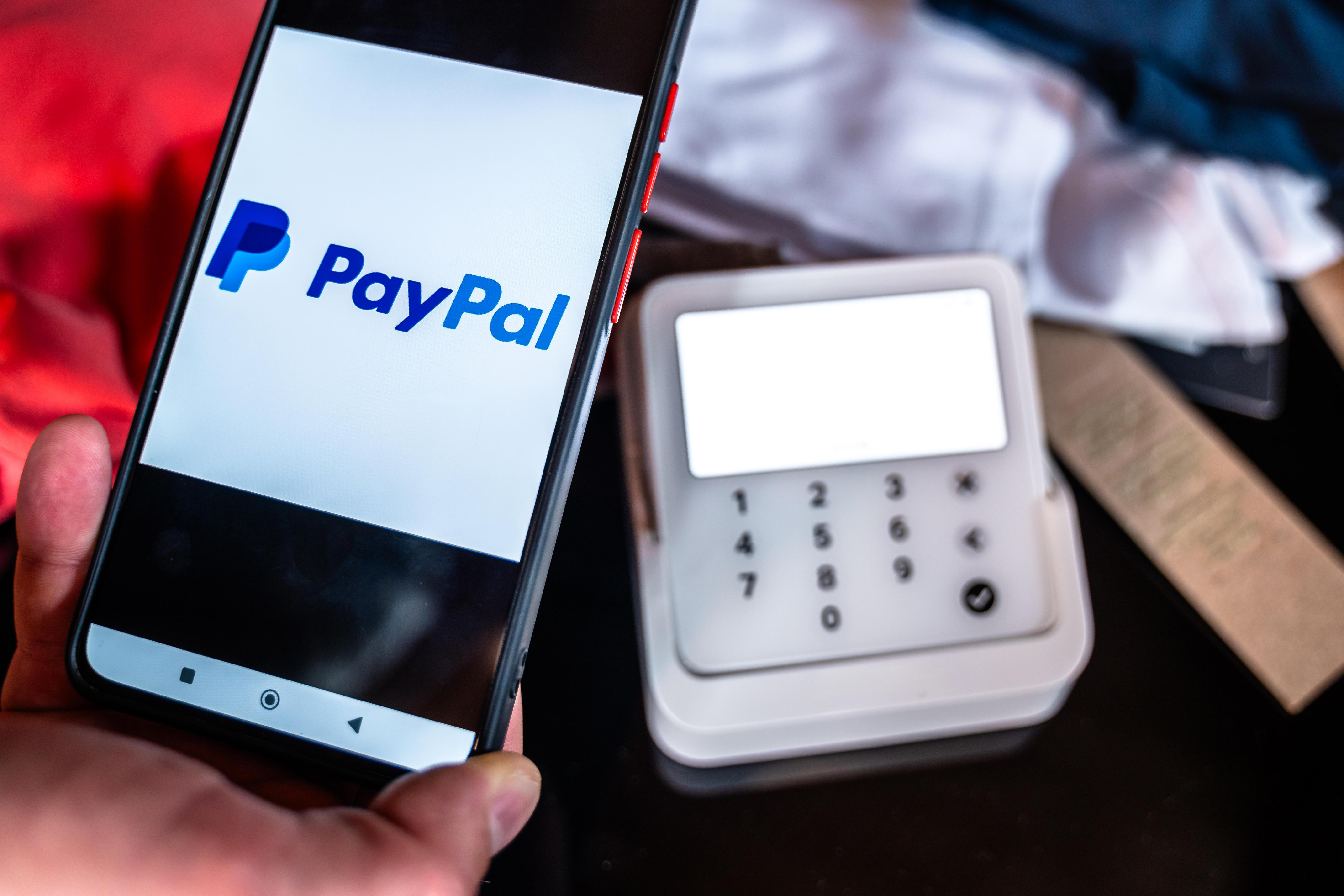 Symbolbild: Ein Kunde bezahlt Kleidung in einem Geschäft mit Paypal Pay per Smartphone. 