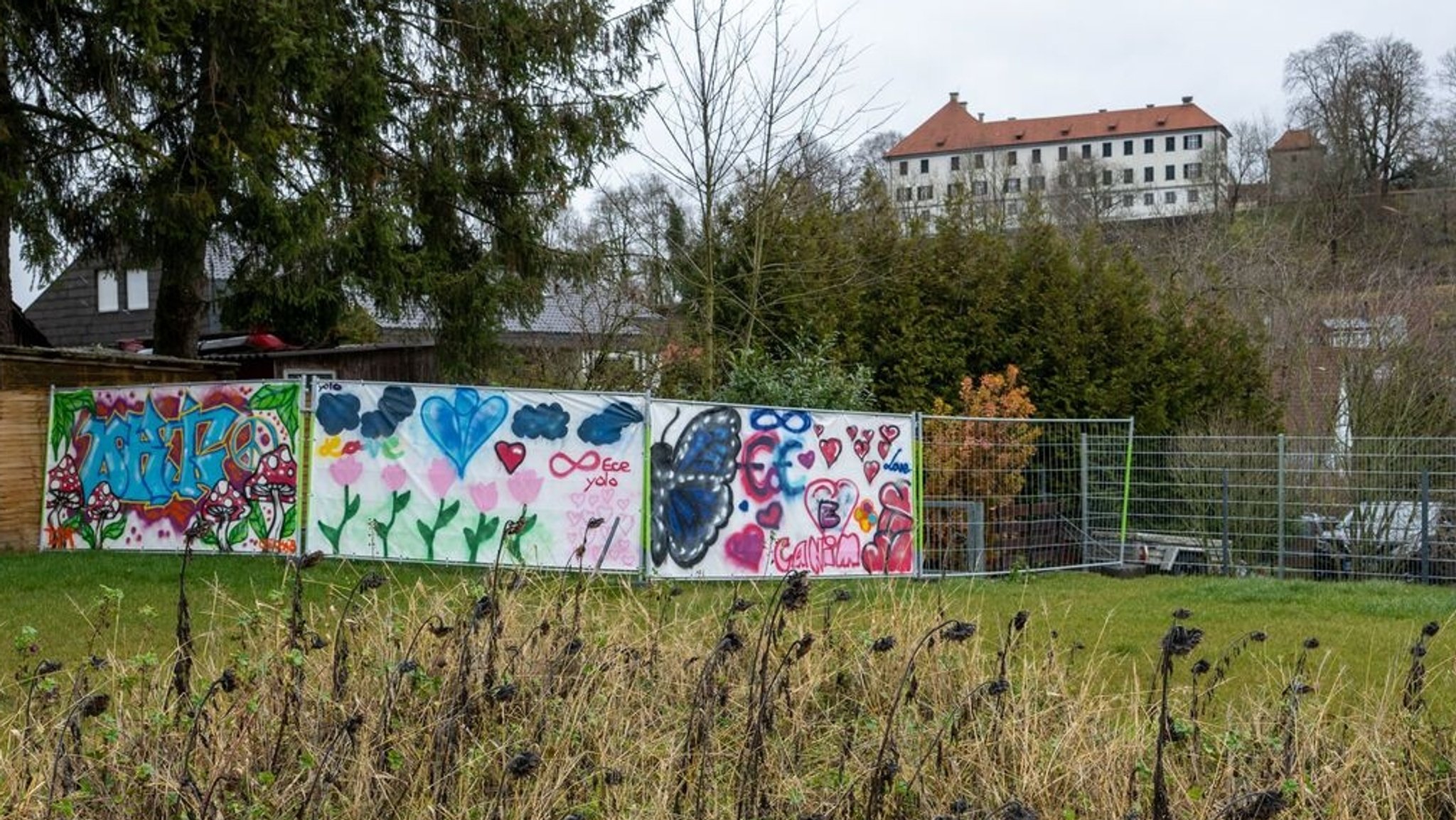 8.11.2023, Baden-Württemberg, Illerkirchberg: An einem Bauzaun hängen bunt bemalte Plakate zum Gedenken an den Messerangriff auf zwei Schülerinnen.