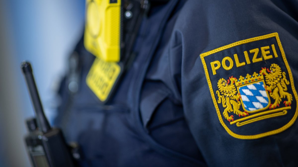 Eine Polizistin trägt ein Polizei-Abzeichen neben einer Body-Cam an einer Schutzkleidung der Klasse 1 (Symbolbild)