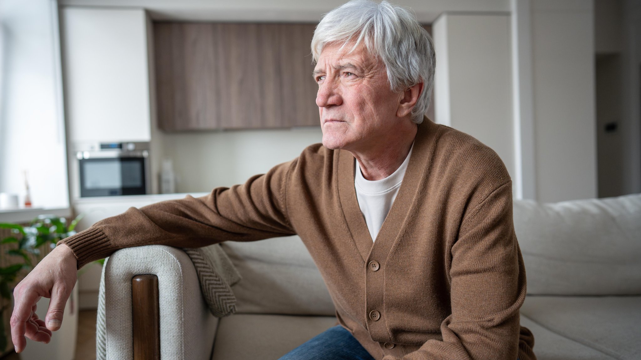 Symbolbild: Ein älterer Mann sitzt auf einem Sofa und sieht nachdenklich in die Ferne.