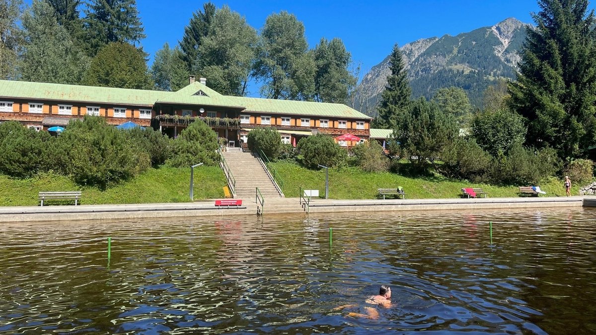 Ein Naturfreibad mit dunkelgrünem Wasser vor einem Alpenpanorama