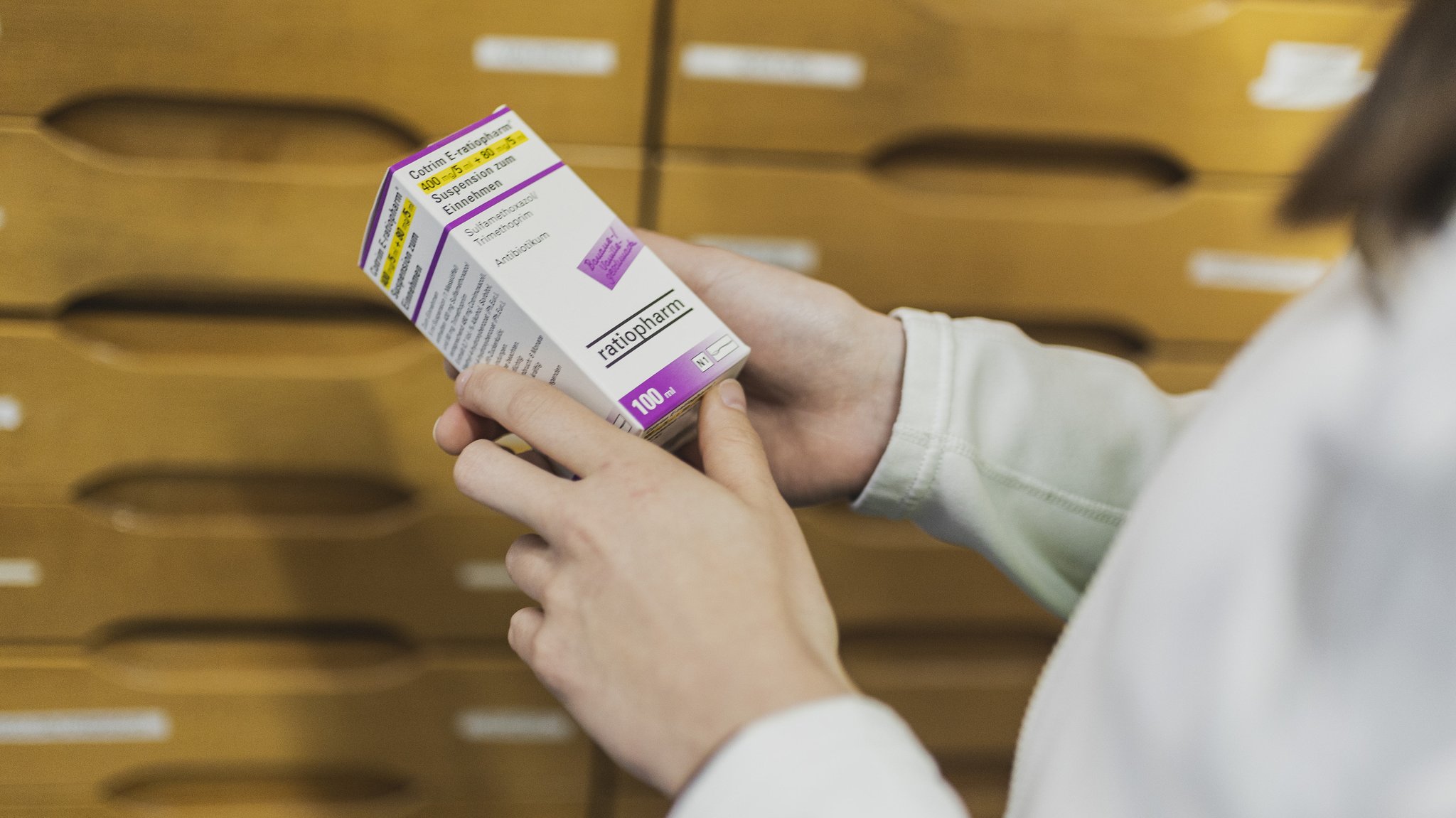 Hände halten Packung mit Antibiotika-Saft für Kinder, aufgenommen in einer Apotheke