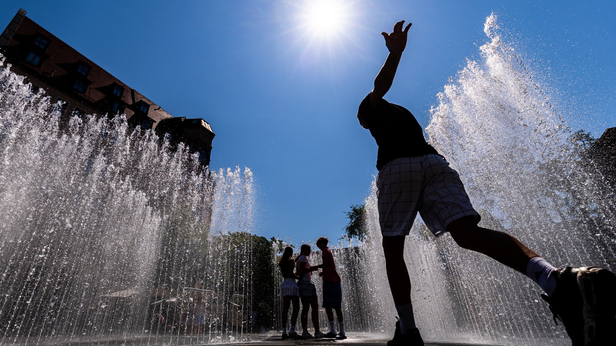 Symbolbild: Hitze in Bayern - Jugendliche laufen durch eine Wasserinstallation 