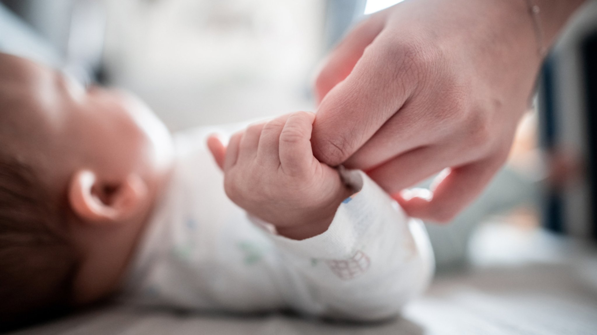 Ein Baby klammert sich an den Finger seiner Mutter. 