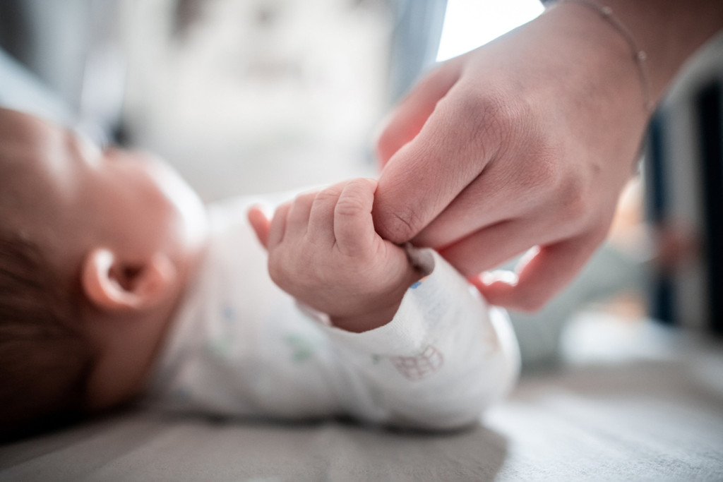 Ein Baby klammert sich an den Finger seiner Mutter. 