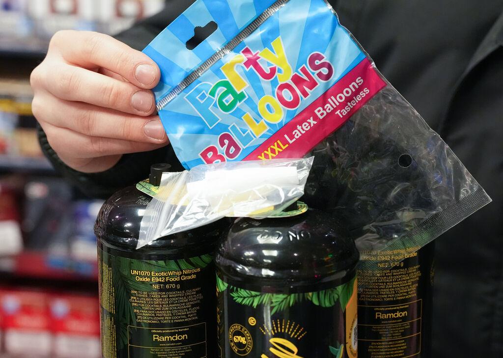 Archivbild: Ein Mitarbeiter hält eine Tüte mit Luftballons, im Vordergrund drei Dosen Lachgas und ein Mundstück