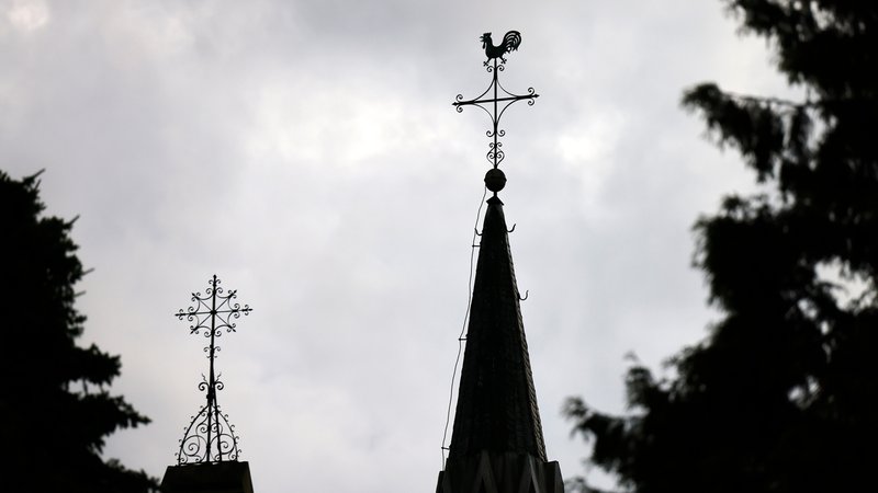 Ein Kreuz mit Wetterhahn steht auf dem Dach einer Kirche vor Wolkenhimmel. | Bild: picture alliance / Panama Pictures | Christoph Hardt Ein Kreuz mit Wetterhahn steht auf dem Dach einer Kirche vor Wolkenhimmel.