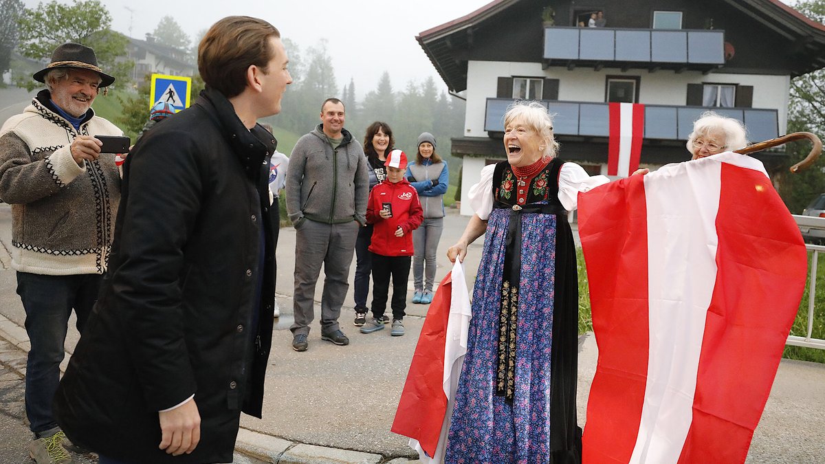 Bundeskanzler Kurz grüßt Dorfbewohner. Eine Frau trägt eine österreichische Flagge.