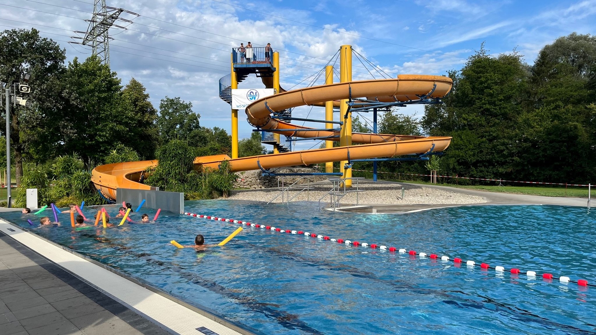 Wasserrutsche und Kinder mit Schwimmnudeln im Becken