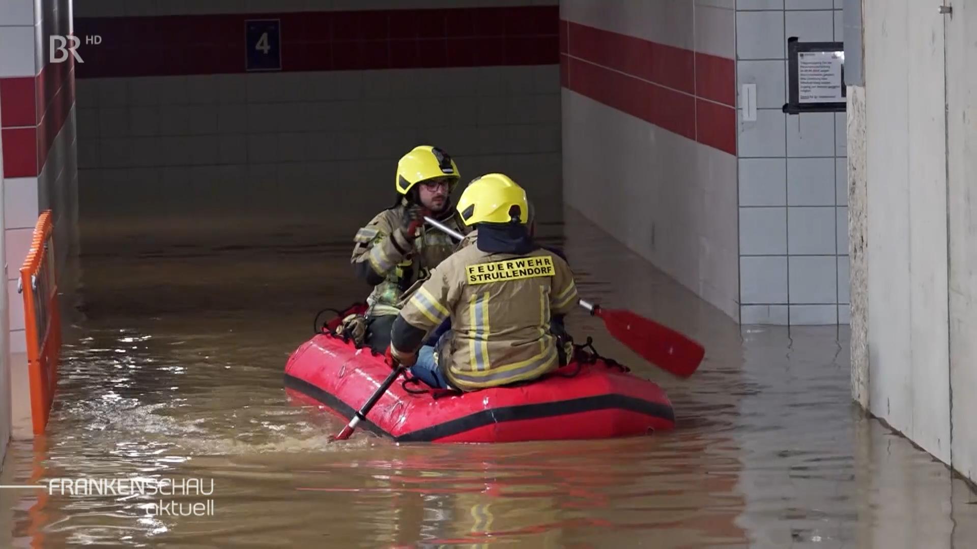 In einem roten Schlauchboot paddeln zwei Feuerwehrleute durch eine überflutete Unterführung. 