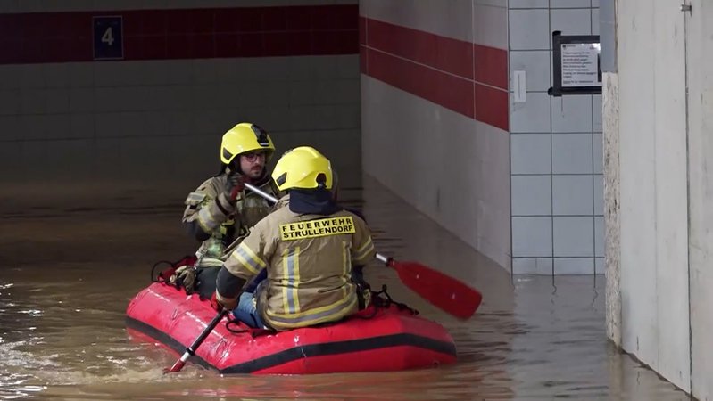 In einem roten Schlauchboot paddeln zwei Feuerwehrleute durch eine überflutete Unterführung. 