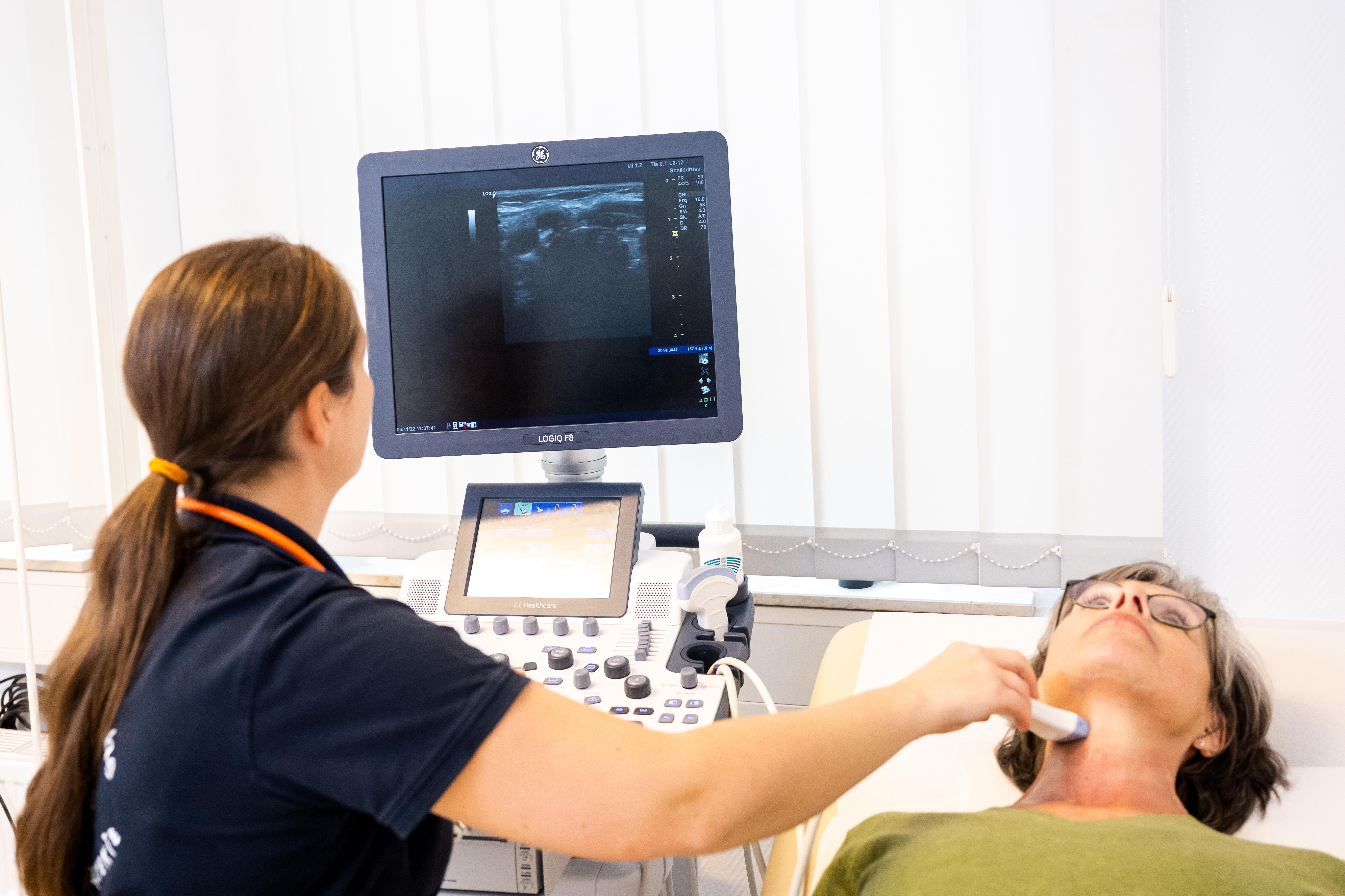 Eine Hausäürztin führt in der Praxis eine Ultraschalluntersuchung der Schilddrüse bei einer Patientin durch