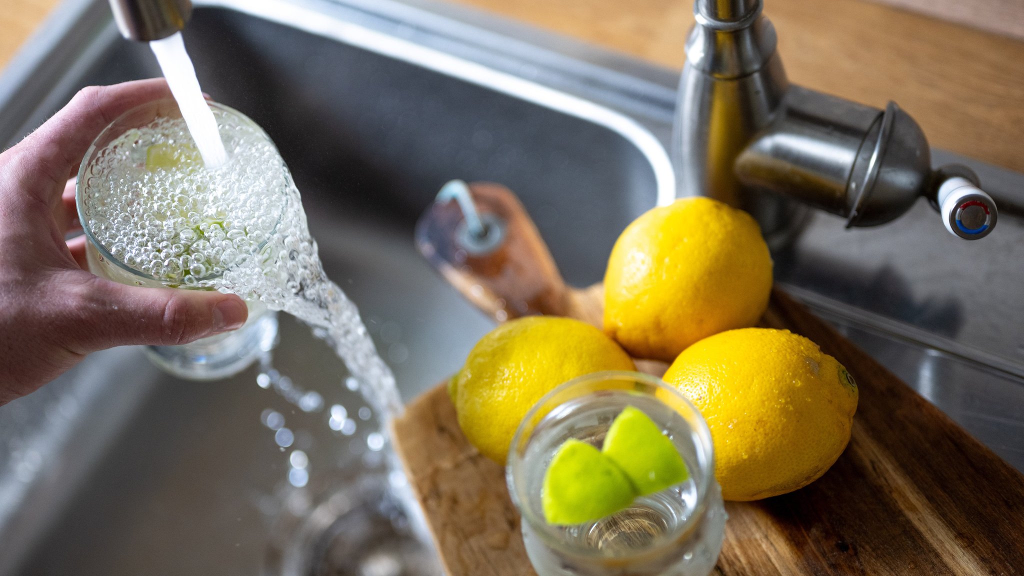 Wasser läuft aus einem Wasserhahn in ein Trinkglas. 