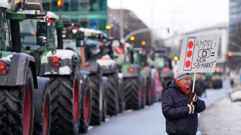 Ein Teilnehmer hält ein Plakat mit der Aufschrift "Ampel: D = Kein SB-Markt" vor Traktoren nach einer Sternfahrt im Rahmen der Aktionswoche des Bauernverbands in der Hamburger Innenstadt hoch.
