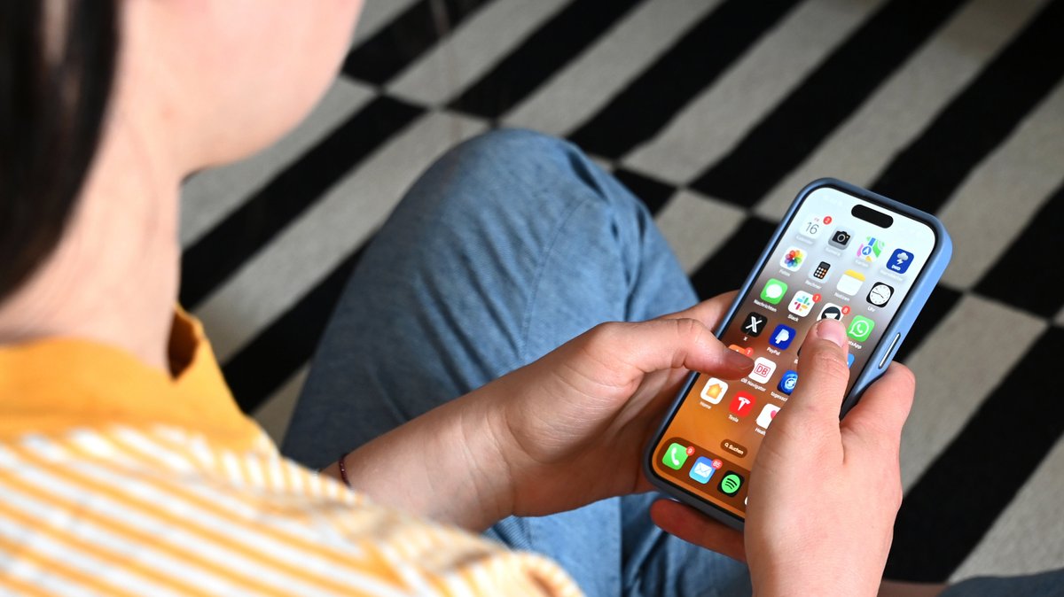 Eine Jugendliche sitzt auf dem Boden und nutzt ein Smartphone - auf dem Display sind verschiedene Apps zu sehen.