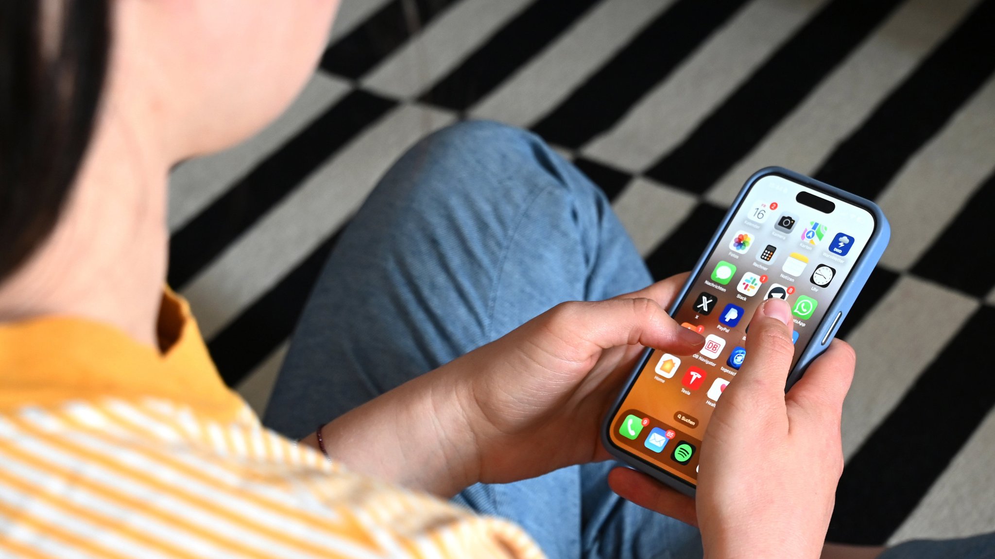 Eine Jugendliche sitzt auf dem Boden und nutzt ein Smartphone - auf dem Display sind verschiedene Apps zu sehen.