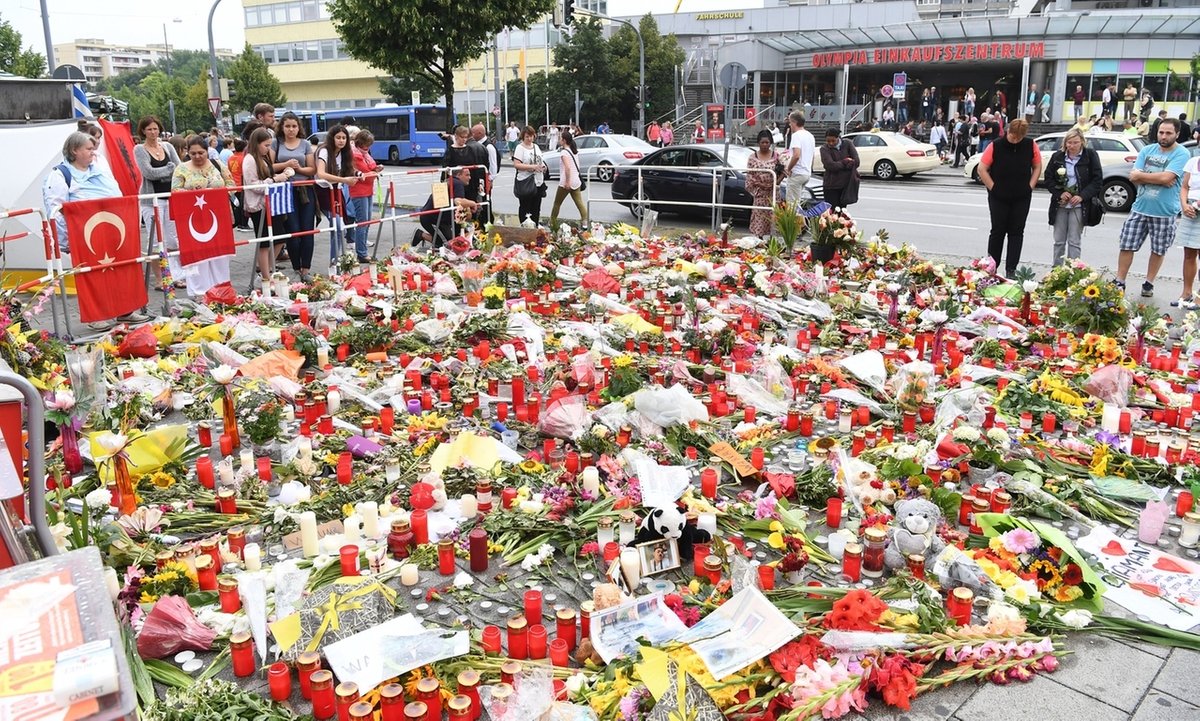 ARCHIV - 25.07.2016, Bayern, München: Blumen und Kerzen liegen auf dem Gehweg vor dem Olympia-Einkaufszentrums (OEZ) in München (Bayern). Dort hatte am 22. Juli 2016 ein 18-jähriger neun Menschen erschossen. 2018 wurde die Tat als rassistischer Anschlag bewertet. (zu dpa «OEZ-Anschlag von München: Als der Hass neun Menschen tötete») Foto: picture alliance / dpa +++ dpa-Bildfunk +++