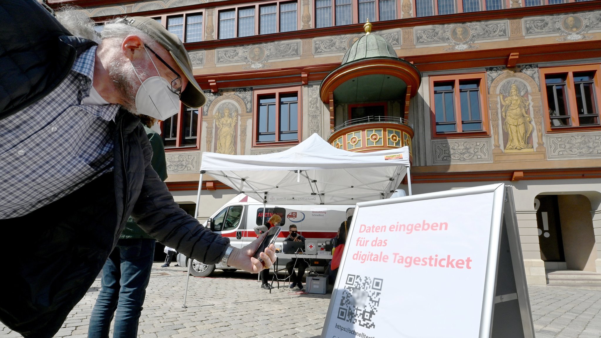 Ein Mann scannt mit seinem Handy in der Innenstadt vor einer Corona Schnelltest-Station einen QR-Code für einen Corona-Schnelltest.