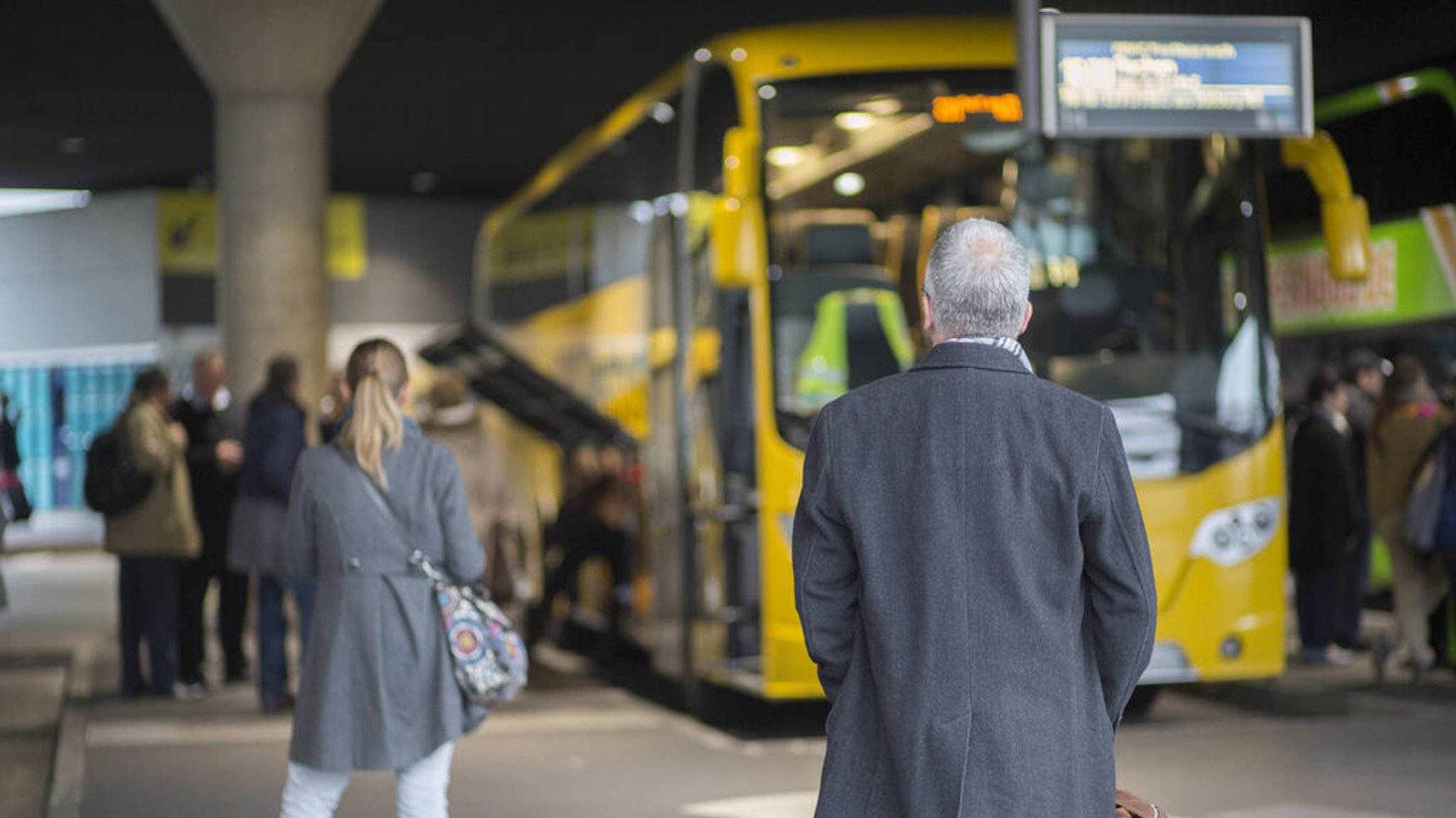 Menschen stehen wartend vor einem gelben Reisebus.