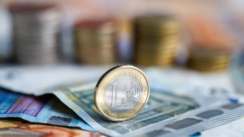 Symbolbild: Eine 1-Euro-Münze, im Hintergrund weitere Münzen und Scheine. | Bild: picture alliance / dpa | Matthias Balk Symbolbild: Eine 1-Euro-Münze, im Hintergrund weitere Münzen und Scheine.