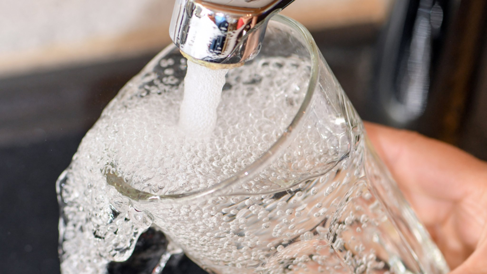 Am Wasserhahn in einer Küche wird ein Trinkglas mit Leitungswasser befüllt.