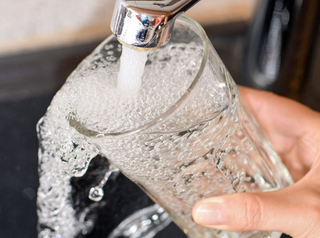 Am Wasserhahn in einer Küche wird ein Trinkglas mit Leitungswasser befüllt.