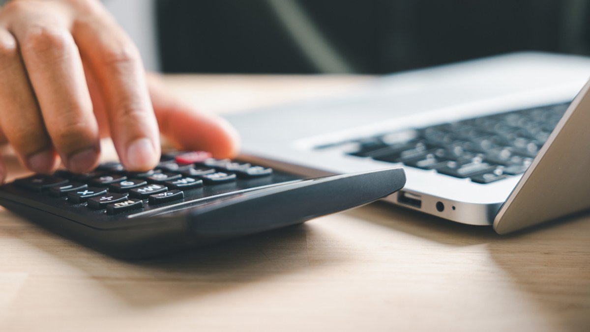 Ein Mann bedient einen Taschenrechner, der neben seinem Laptop liegt.