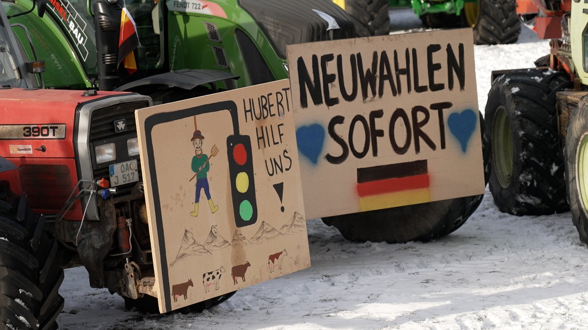 An zwei Traktoren sind Spanplatten befestigt auf denen steht: "Hubert hilf uns" und Neuwahlen sofort"
