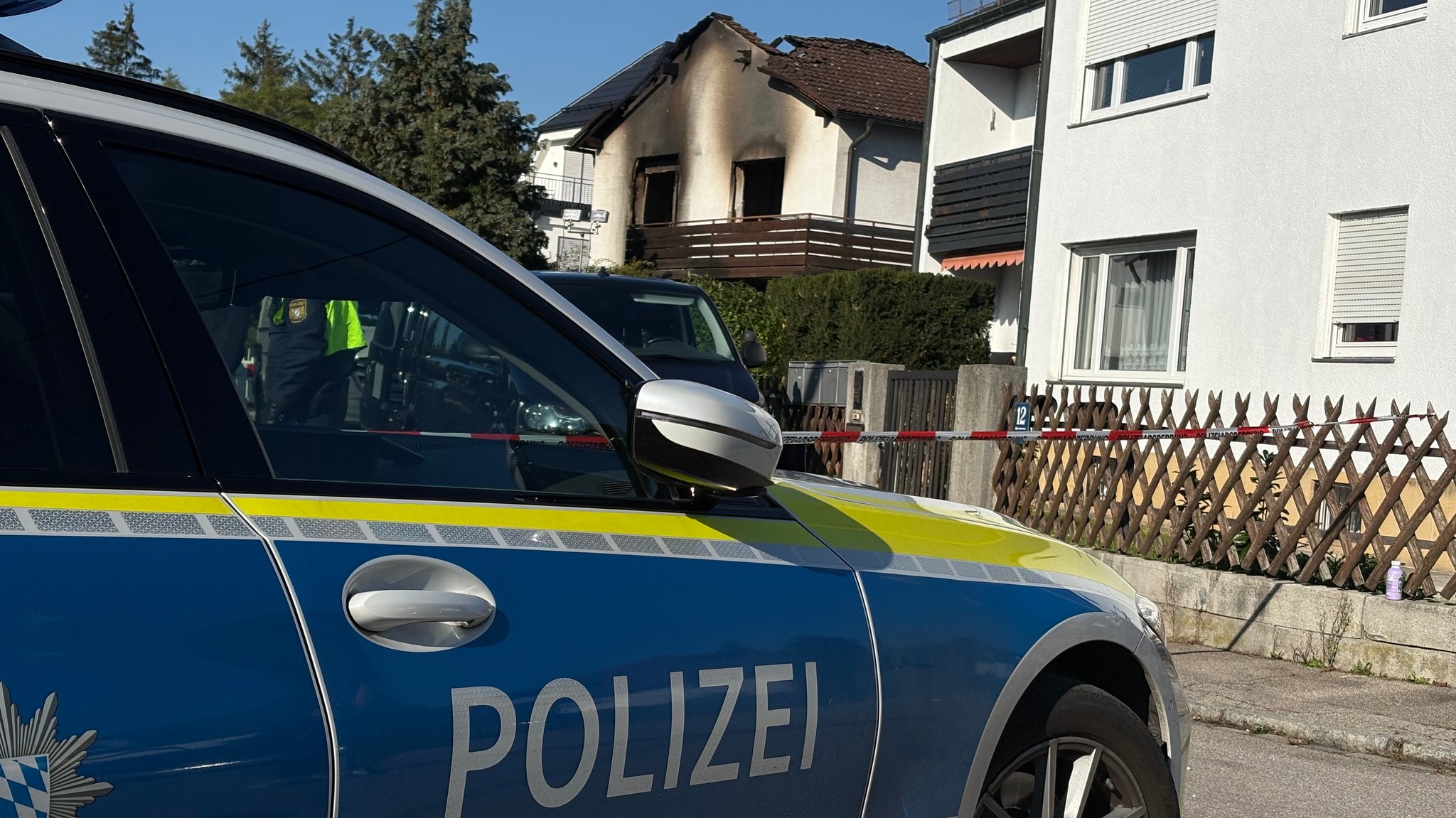Polizei vor abgesperrtem Gehweg vor dem ausgebrannten Einfamilienhaus.