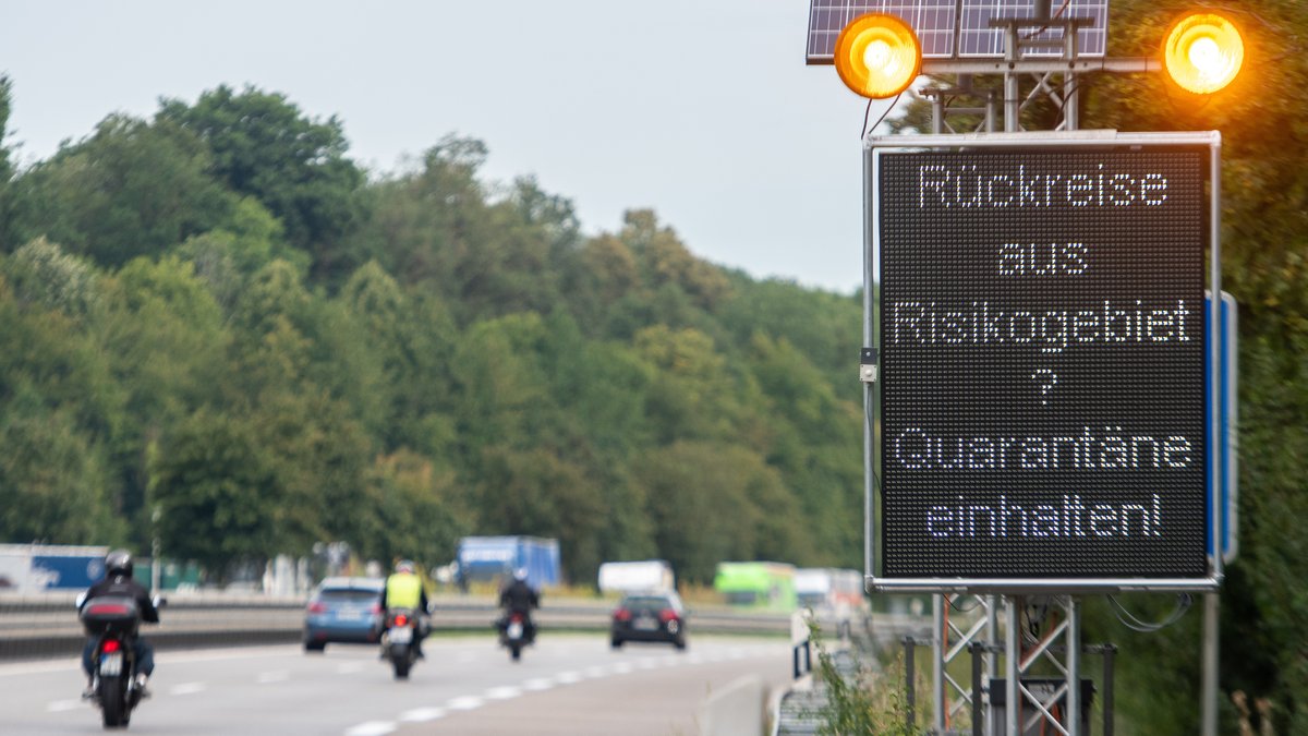 Ein Schild mit der Aufschrift "Rückreise aus Risikogebiet? Quarantäne einhalten!"- neben einer befahrenen Straße
