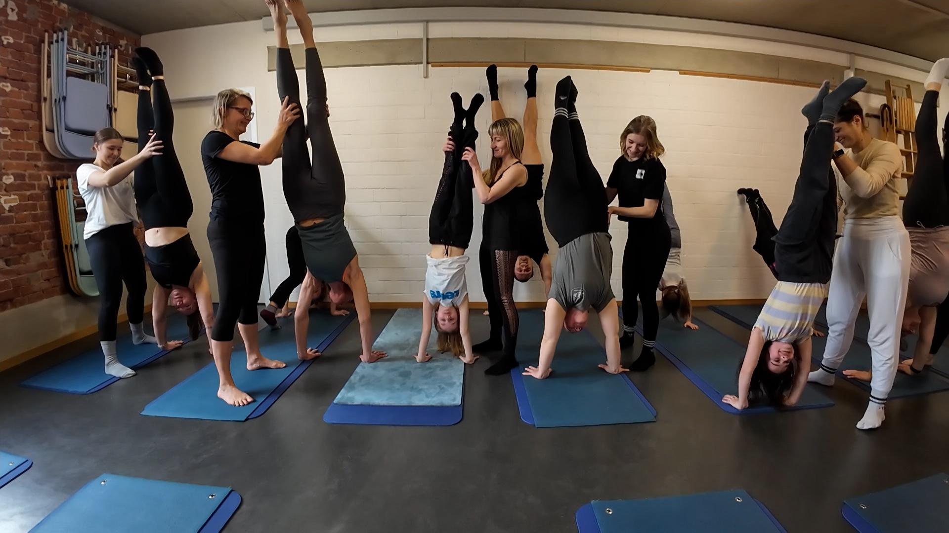 Handstand-Workshop-Teilnehmende stehen mit Hilfestellung anderer Teilnehmender auf ihren Händen.