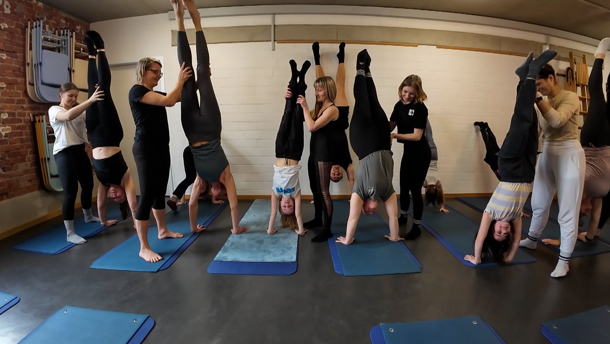 Handstand-Workshop-Teilnehmende stehen mit Hilfestellung anderer Teilnehmender auf ihren Händen.