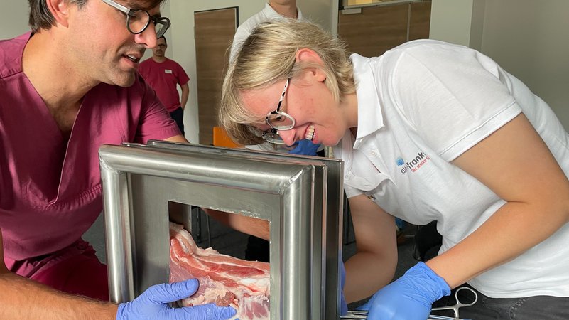 Eine Medizinstudentin legt an einem Schweinebauch eine Thoraxdrainage, ein Arzt leitet sie an.