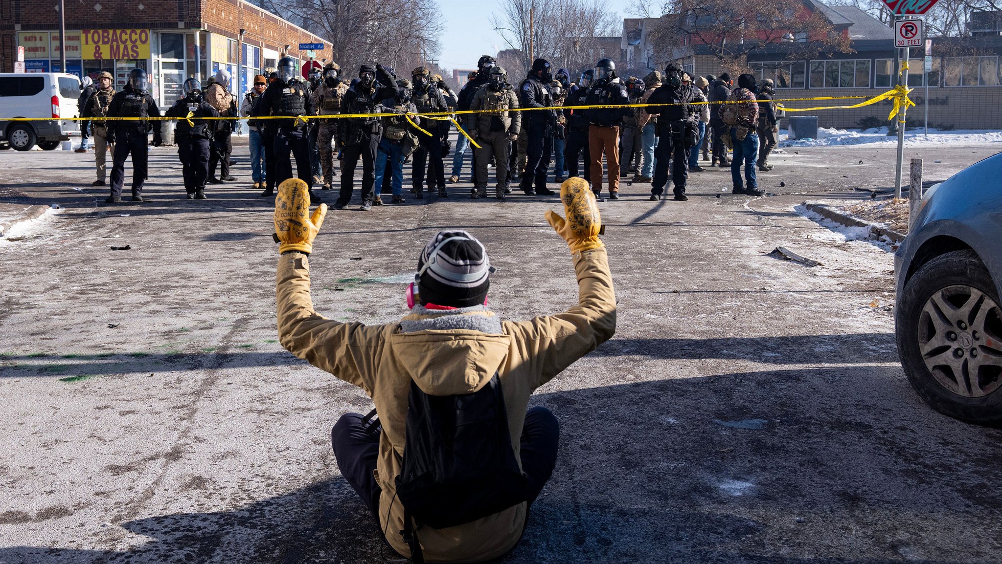 24.01.2026, USA, Minneapolis: Ein Demonstrant sitzt mit erhobenen Armen auf der Straße vor Bundesbeamten in Minneapolis. Foto: Alex Kormann/Star Tribune/AP/dpa - ACHTUNG: Nur zur redaktionellen Verwendung und nur mit vollständiger Nennung des vorstehenden Credits +++ dpa-Bildfunk +++
