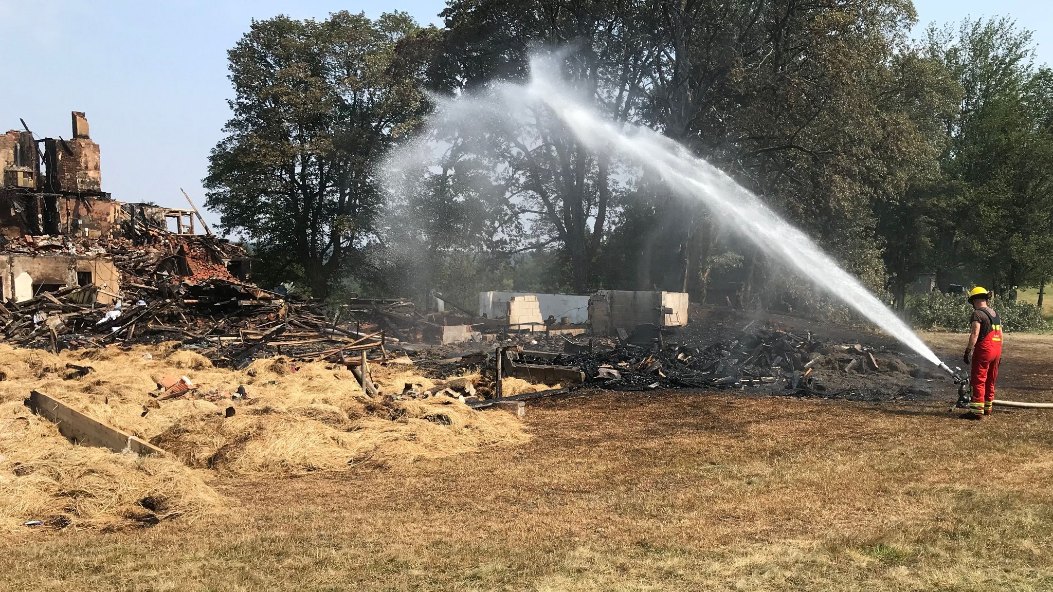 Ein Feuerwehrmann löscht die Brandruine des Bauernhofes.